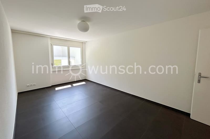 Empty room with dark tiled flooring, white walls, a large window with glass panels, and a single ceiling light fixture.
