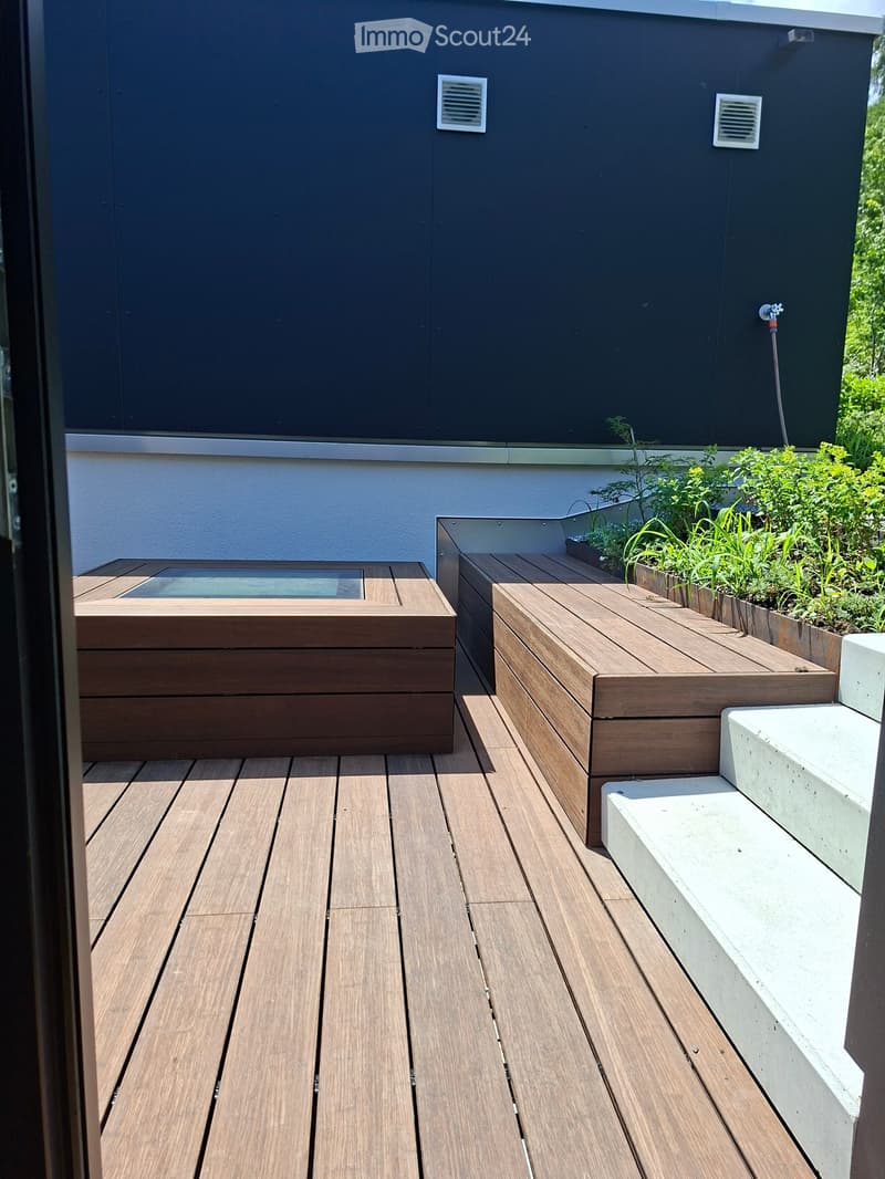 Wooden deck with built-in seating and small raised garden bed, featuring a modern design with dark walls and white accents.