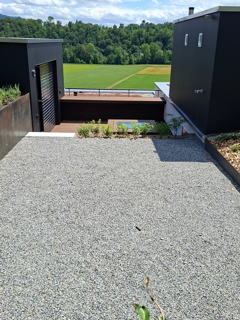 Modern rooftop terrace with gravel surface, wooden deck, small pool, and surrounding greenery.