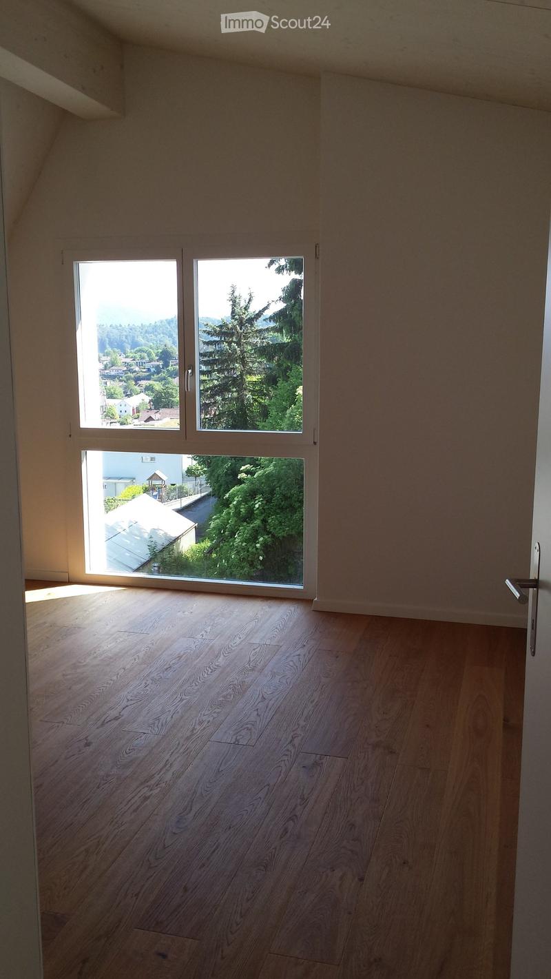Empty room with wooden flooring and large windows offering a scenic view of trees and houses.
