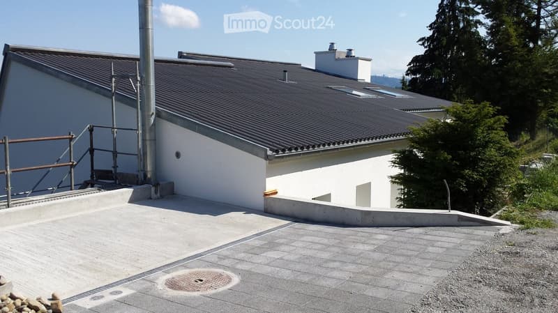 Modern building with a raised ground floor, grey tiled roof, white walls, and a small staircase leading up to the entrance.