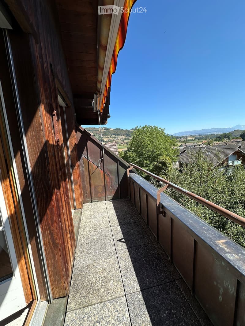 Balcony with tiled floor, wooden railing, and scenic view of countryside and mountains.