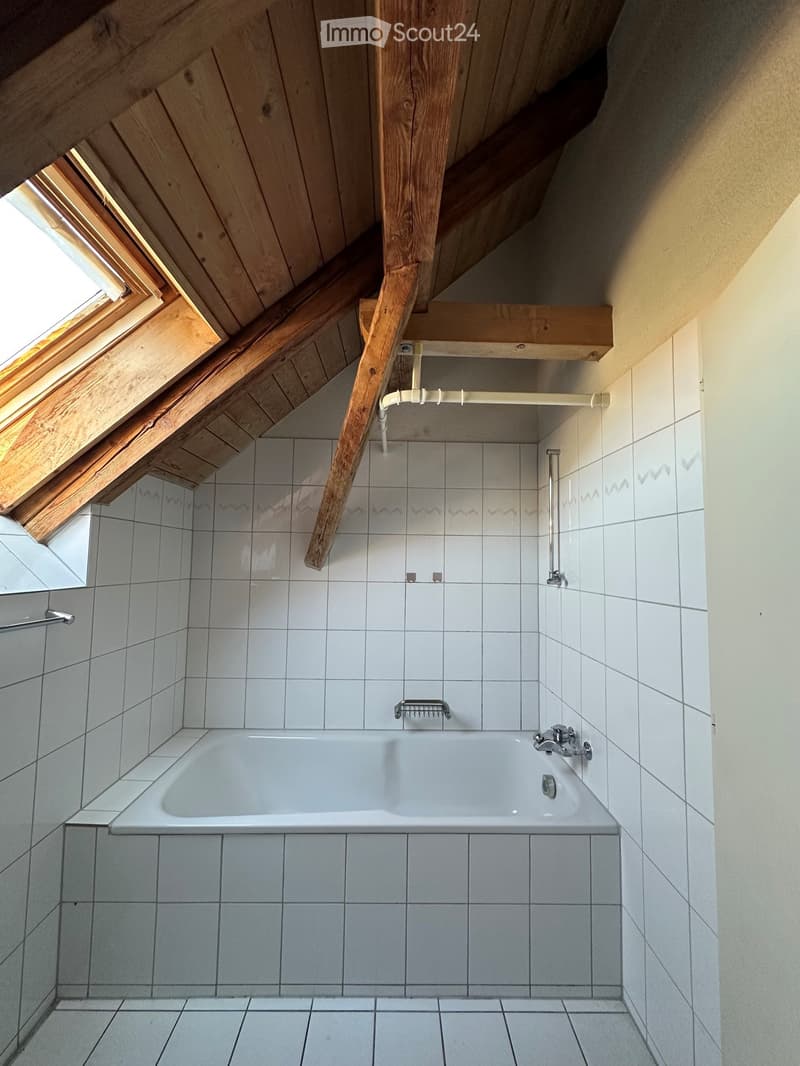 Modern bathroom with a white tiled wall and floor, a bathtub, and a skylight window above the tub.