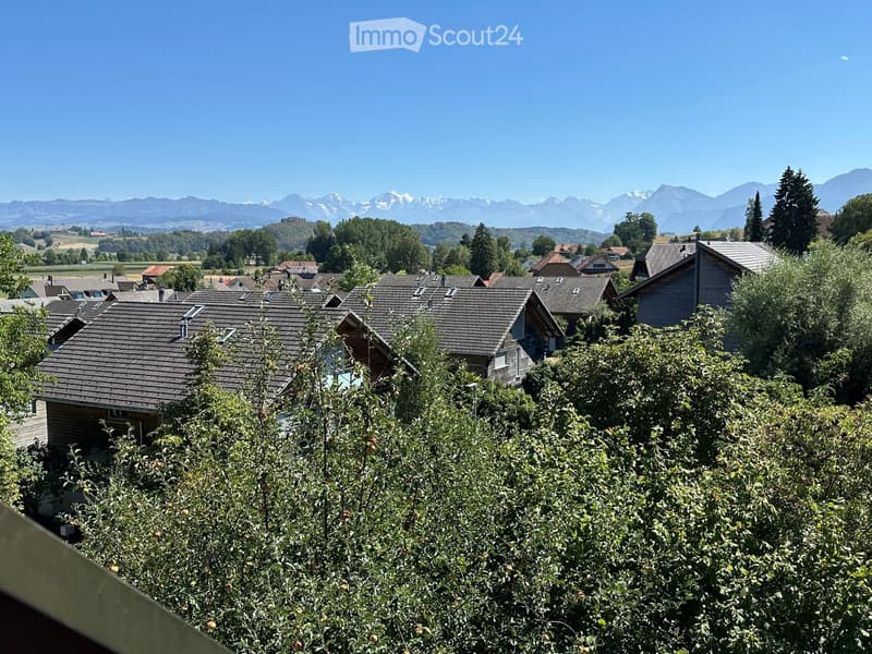 A view of a residential area with houses, trees, and a distant mountain range under a clear blue sky.