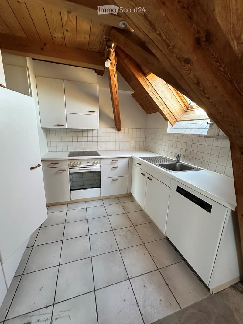 Modern kitchen with white cabinets, stainless steel sink, oven, and tiled floor. Features exposed wooden beams and a skylight window.