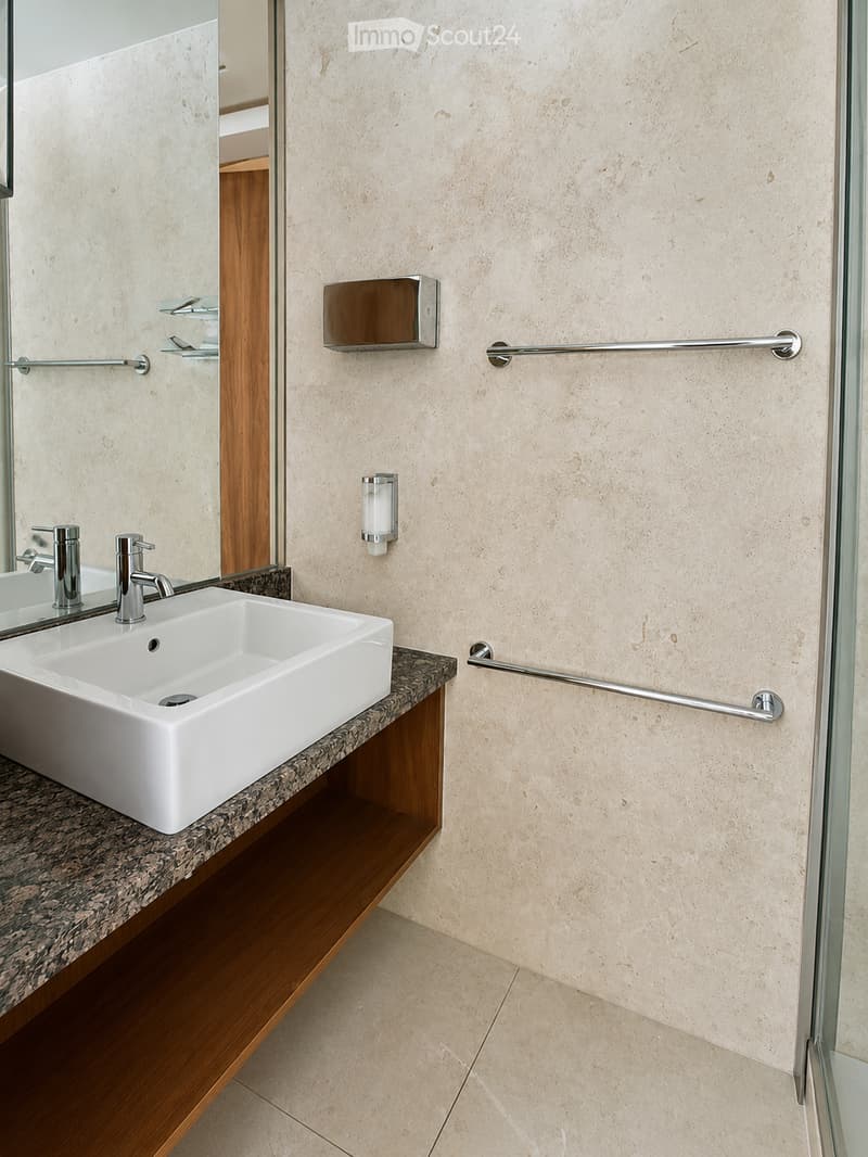 Modern bathroom with a white sink, chrome faucet, granite countertop, and a large mirror. Beige tiled walls and a wooden cabinet base.