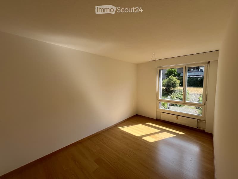 Empty room with wooden flooring and large windows, allowing natural light to illuminate the space.