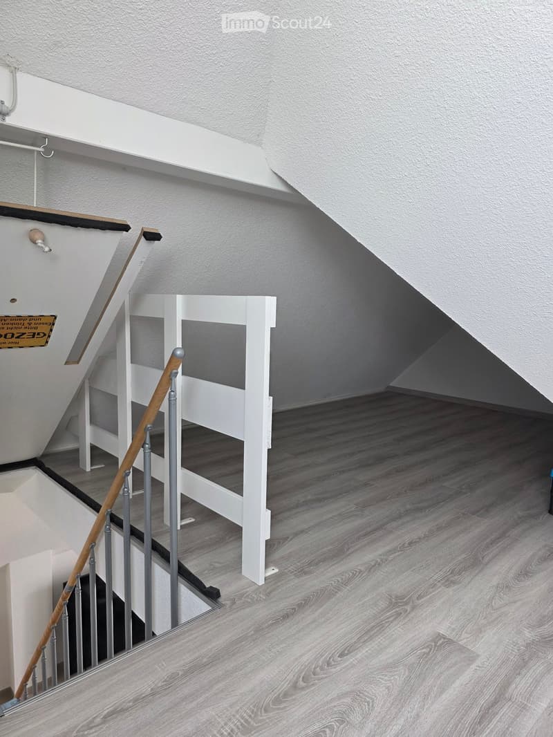 Modern hallway with wooden flooring, white walls, and a staircase featuring a wooden handrail and white balusters.
