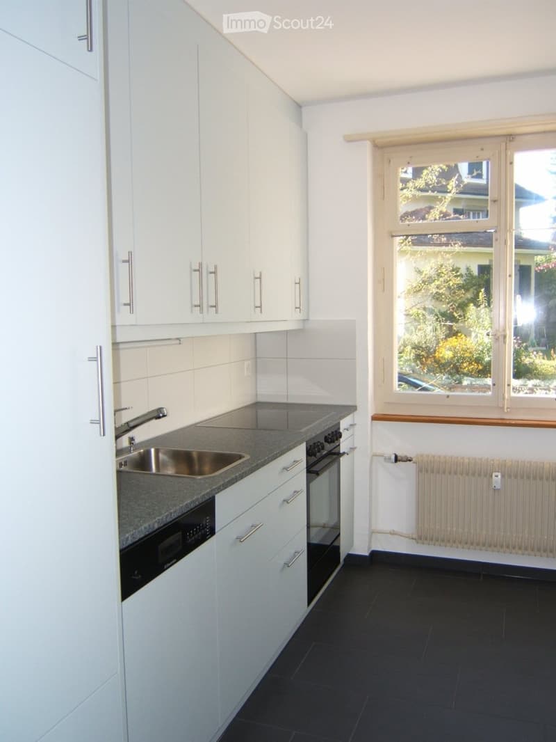 Modern kitchen with white cabinets, stainless steel sink, oven, microwave, and dark tiled floor.