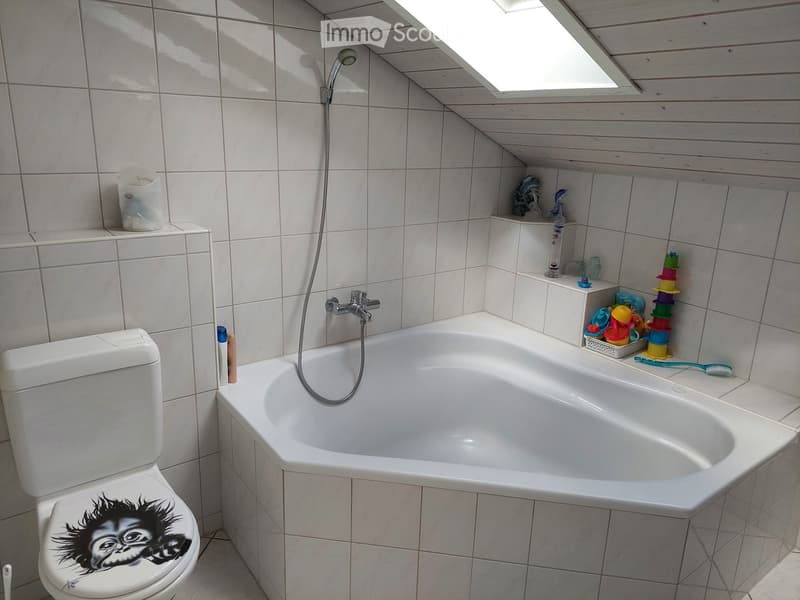 Bathroom with a bathtub, toilet, and showerhead. The walls are tiled, and there are various toiletries and toys on the edge of the bathtub.