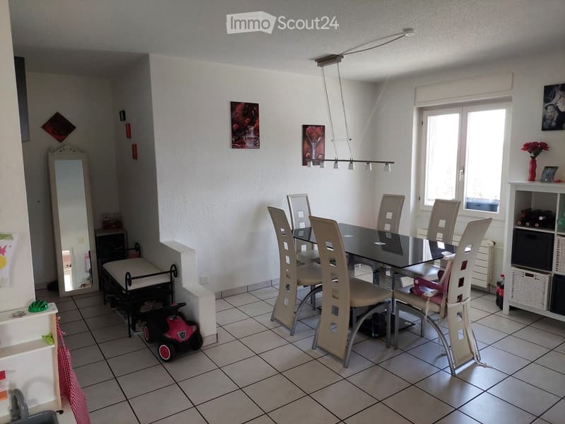 Dining room with a black dining table surrounded by six chairs, a large mirror on the wall, a shelf with decorative items, and a small child's toy car on the floor.