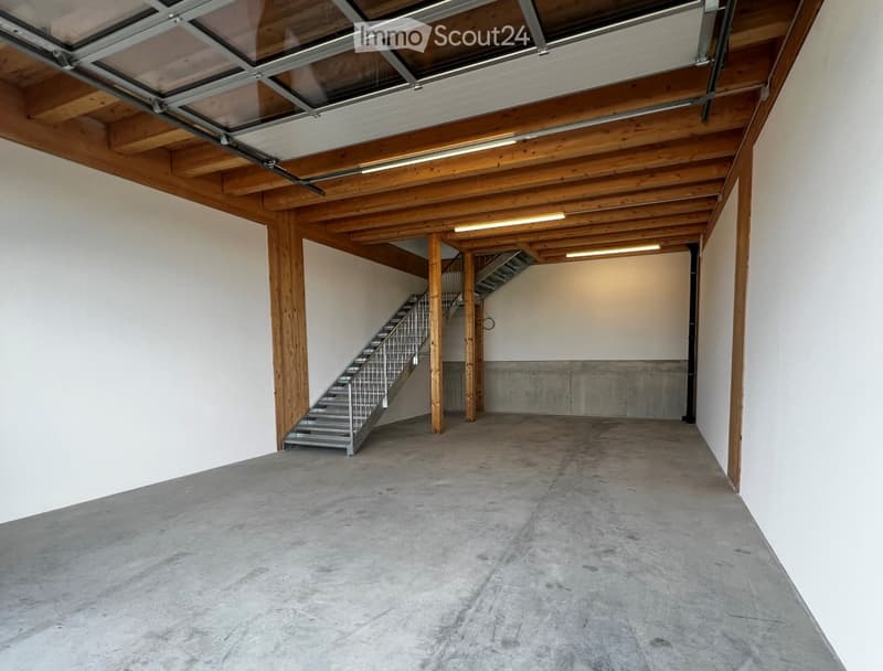 Empty garage with concrete floor, wooden beams, metal staircase leading to an upper level, and a skylight in the ceiling.
