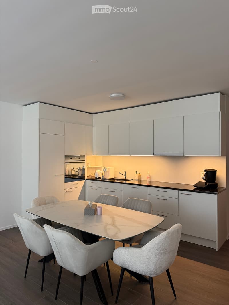 Modern kitchen with white cabinets, a dining table with six chairs, and various appliances including a coffee maker and oven.