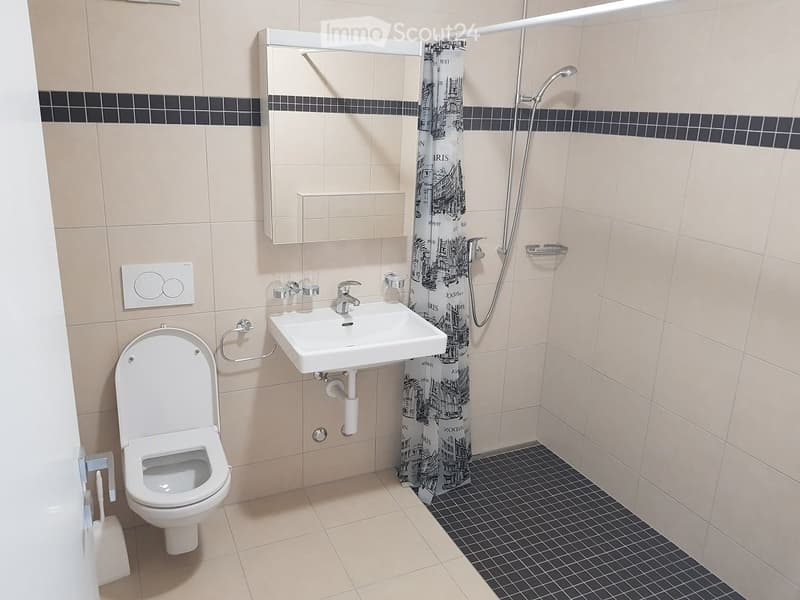 Modern bathroom with beige tiles, a white toilet, a sink with a mirror above it, and a shower area with a decorative black-and-white patterned curtain.