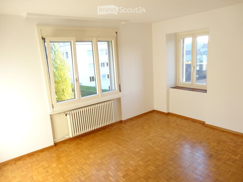 Empty room with wooden flooring, white walls, large windows, and radiators.