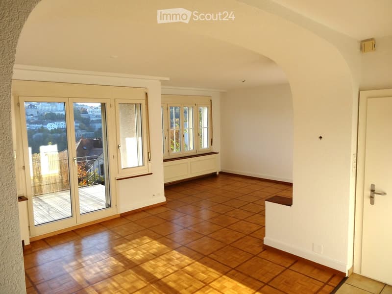 Empty room with wooden flooring, large windows, and a sliding glass door leading to a balcony with a city view.
