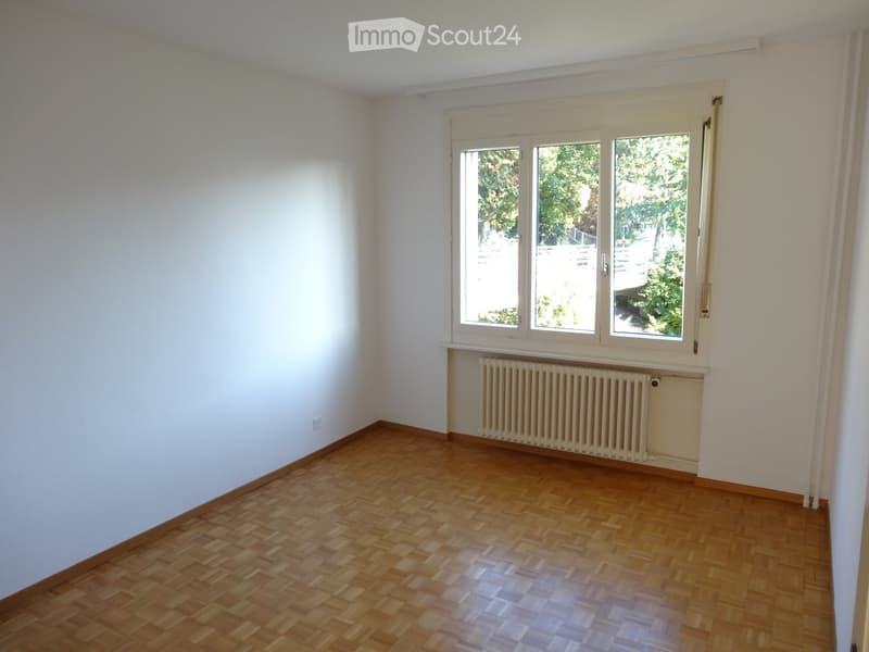 Empty room with wooden flooring, white walls, and large windows with a radiator below them.