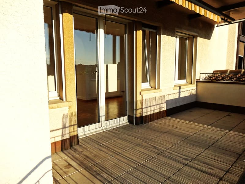 Balcony with tiled flooring, large glass sliding doors leading to an interior space, and a covered section with a yellow awning.