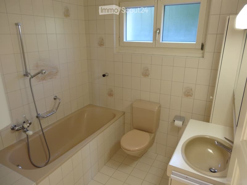 Bathroom with beige tiles, bathtub, toilet, sink, and shower hose.