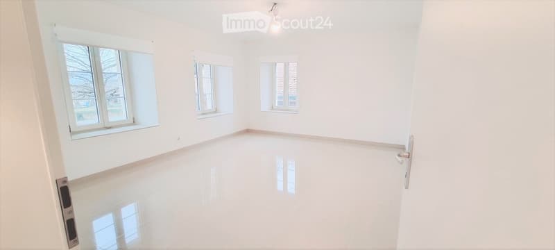 Empty room with white walls, polished white floor, and multiple windows allowing natural light.