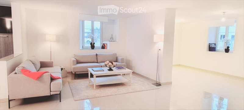 Modern living room with white walls, large windows, grey sofa, coffee table, and floor lamps.