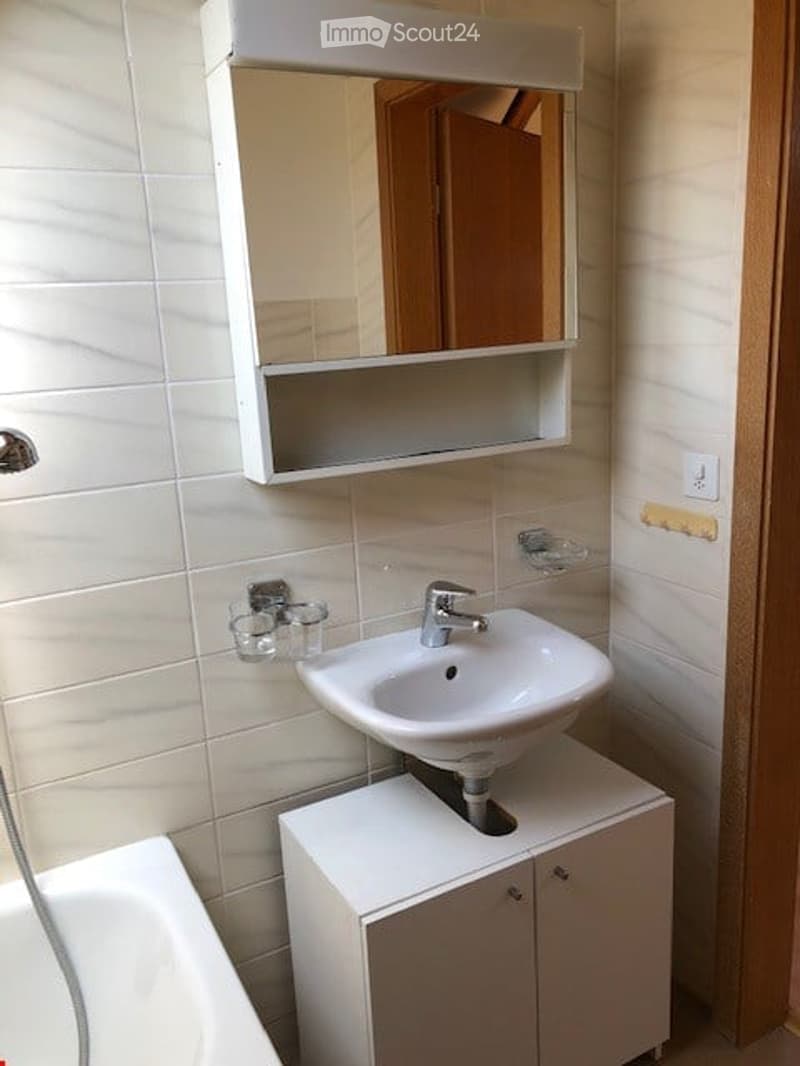 Modern bathroom with white tiles, a white sink on a cabinet, a mirror cabinet above, and a toothbrush holder on the wall.