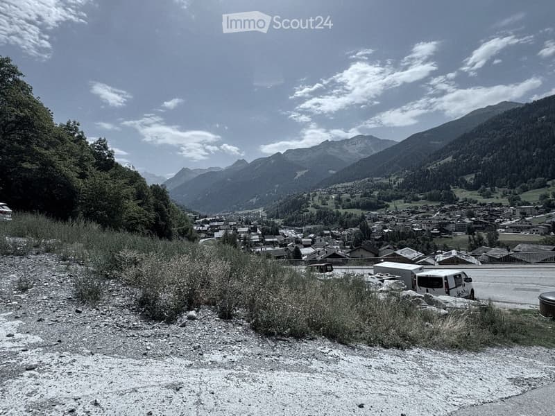 A scenic mountain view with a small village nestled in a valley, surrounded by lush greenery and rocky terrain.