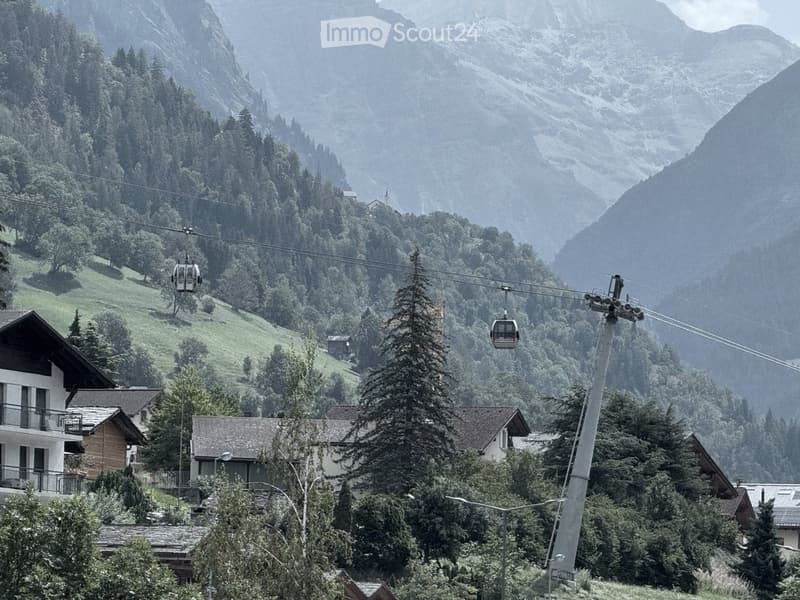 A scenic mountain valley with a cable car system running through it, surrounded by dense forests and traditional houses.