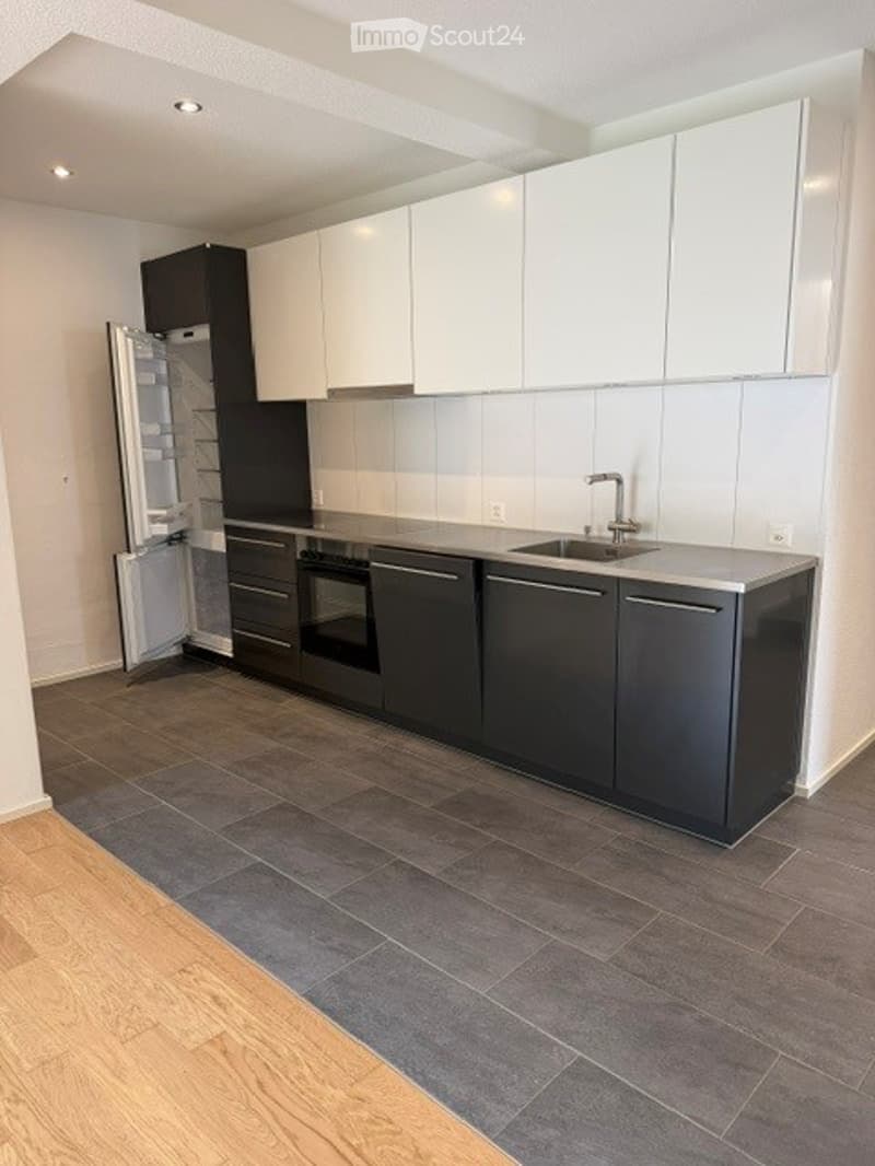 Modern kitchen with white upper cabinets, black lower cabinets, stainless steel appliances, and a gray countertop.