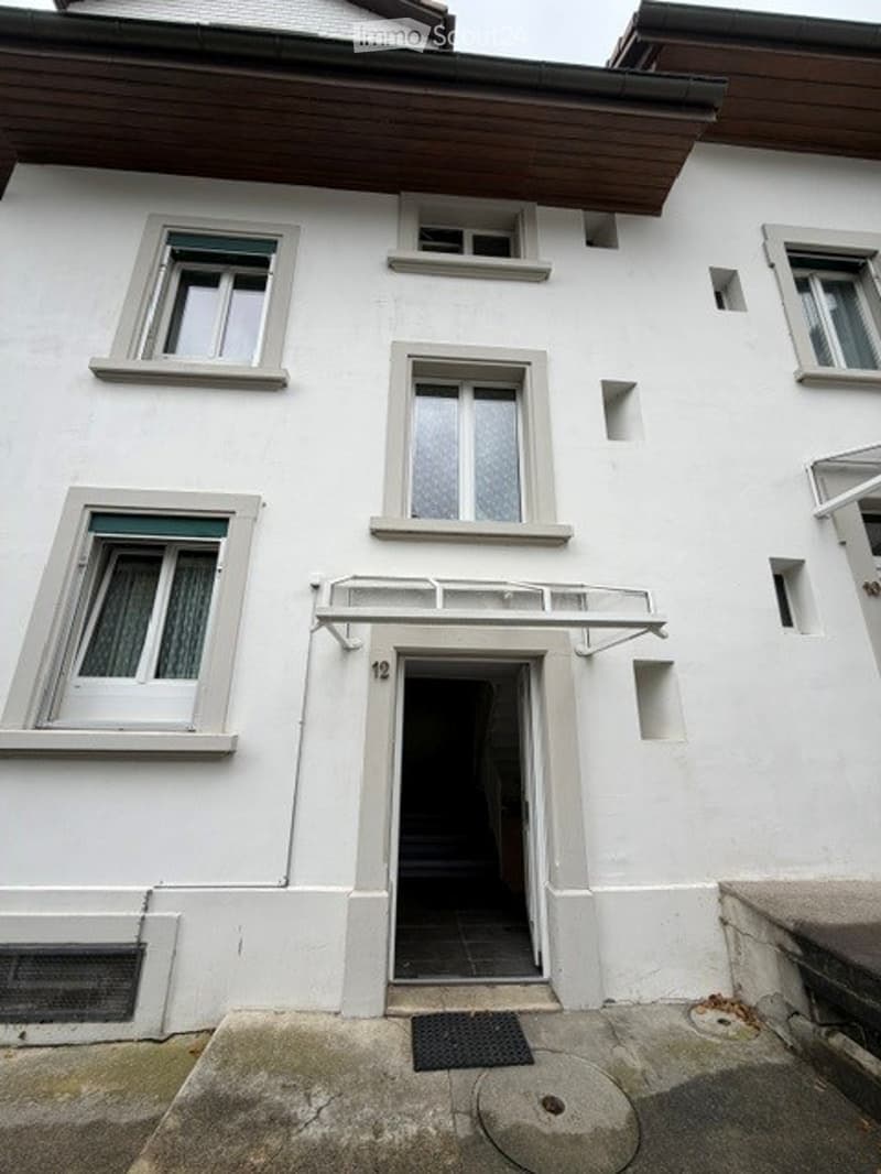 A multi-story residential building with white exterior walls, multiple windows, and a central entrance marked with the number 12.