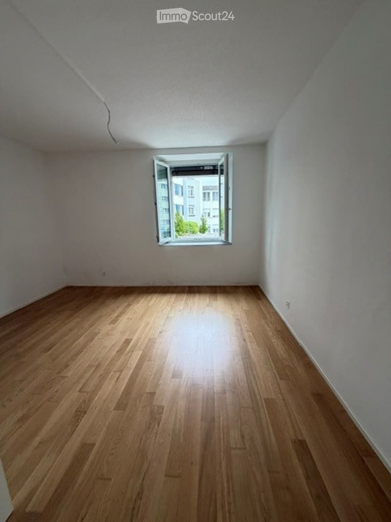 Empty room with wooden flooring and a single window letting in natural light. No furniture or equipment present.