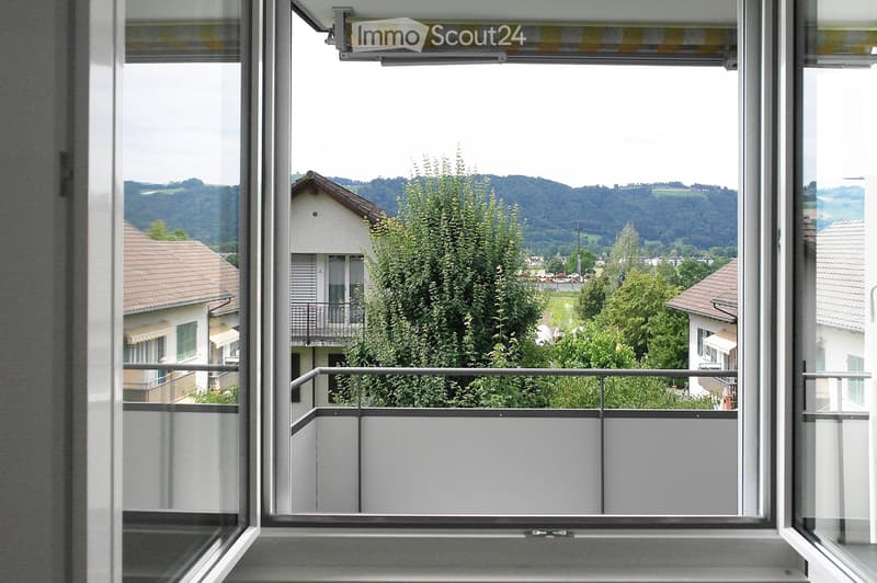 Window view from a balcony, overlooking a tree, a building with a balcony, and mountains in the distance