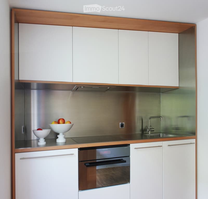 White cabinetry, stainless steel backsplash, built-in dishwasher, gas stove, sink with faucet, white bowl with apples on counter