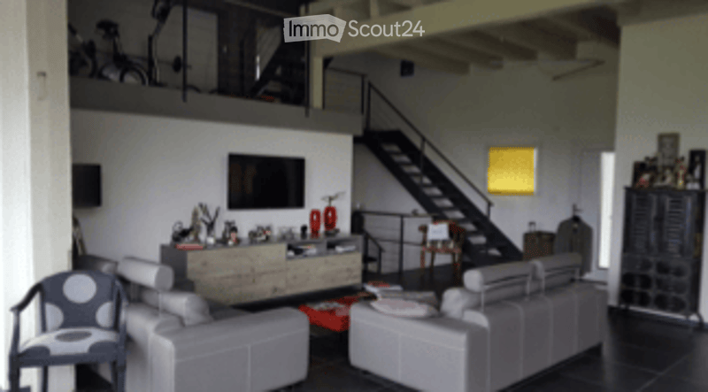 Modern living room with grey sofas, a coffee table, a television, and a lamp. The room features exposed wooden beams and a staircase leading to an upper level.