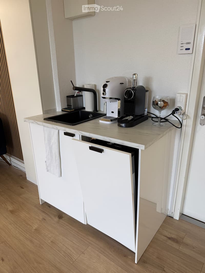 Modern kitchen with white cabinets, marble countertop, sink, coffee machine, and a glass cup on the counter.