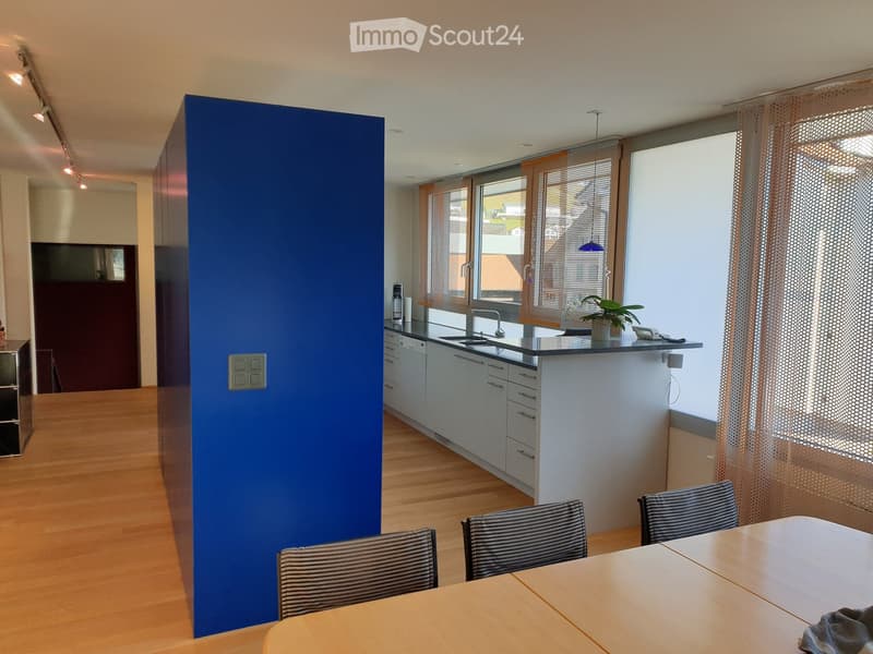 Modern kitchen with white cabinets, a central island, and a dining area with a table and chairs. Features a blue accent wall and large windows with blinds.