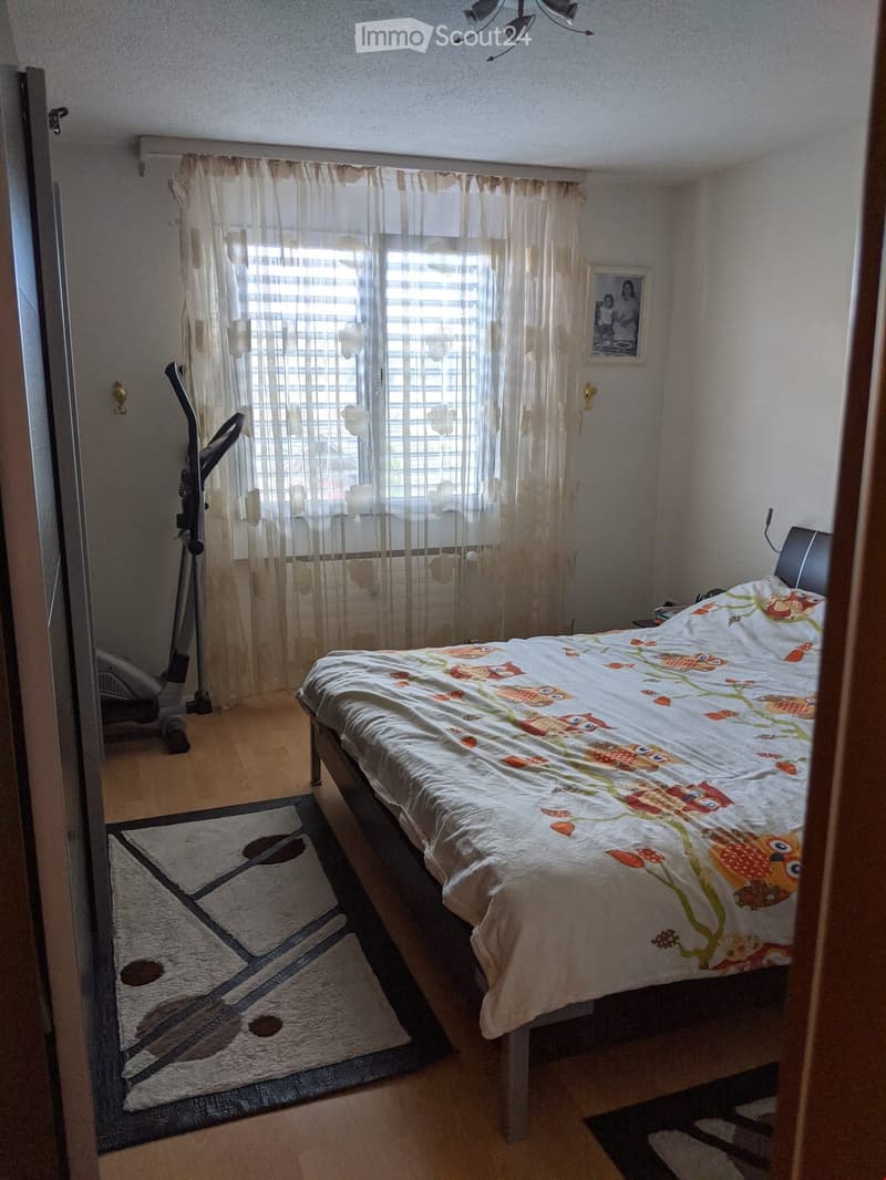 Bedroom with a double bed, owl-patterned duvet, exercise bike, and a patterned rug on the floor.