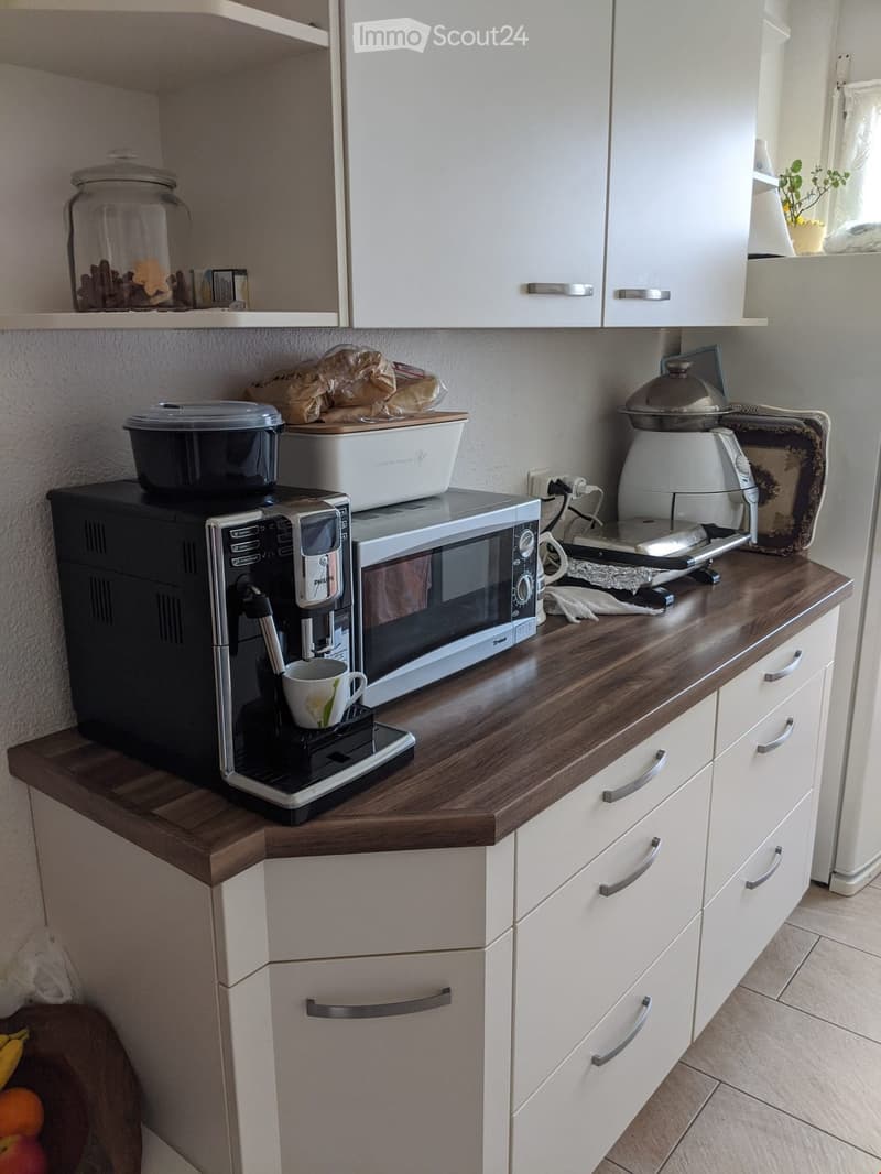 Modern kitchen with white cabinets, wooden countertop, coffee machine, microwave, and various kitchen appliances.