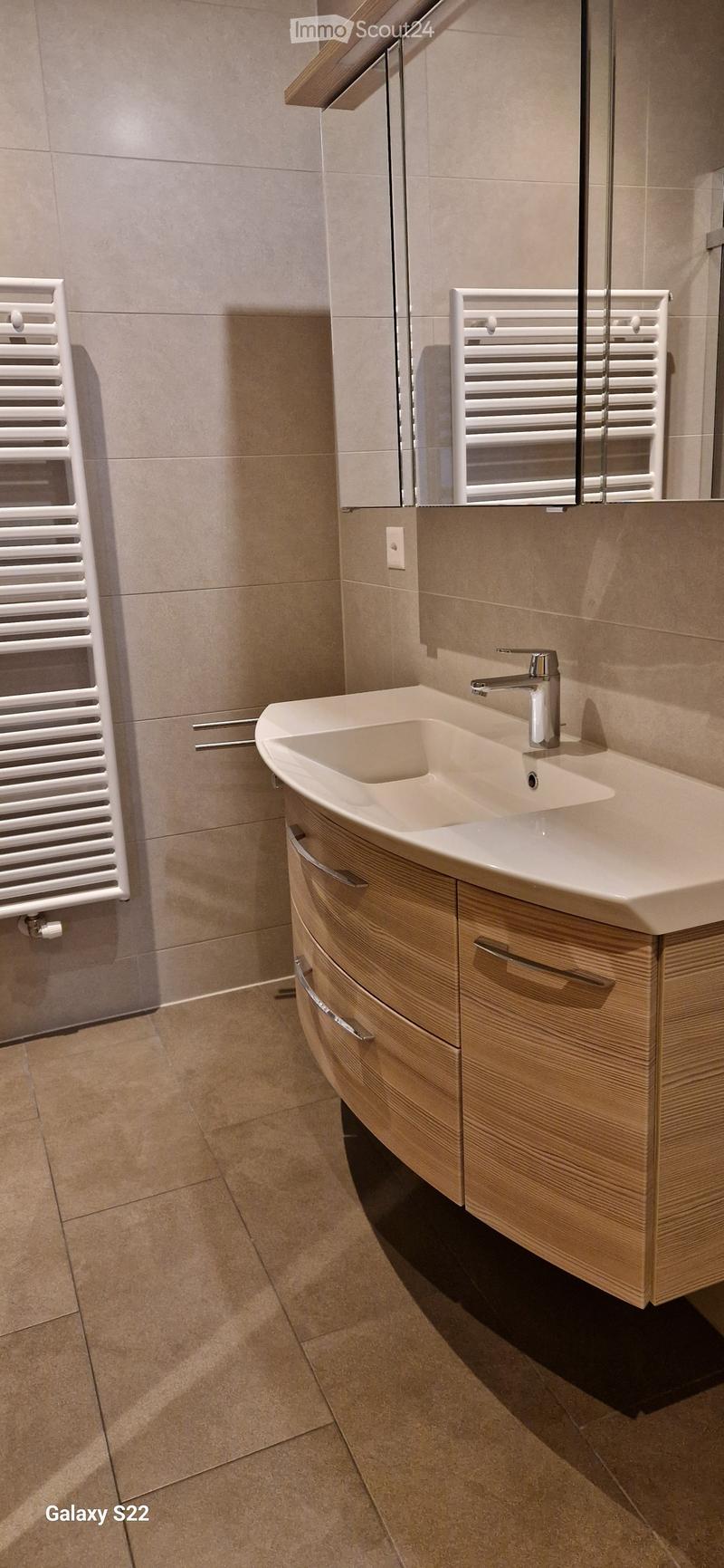 Modern bathroom with a white sink, chrome faucet, wooden cabinet, and a white radiator on the wall.