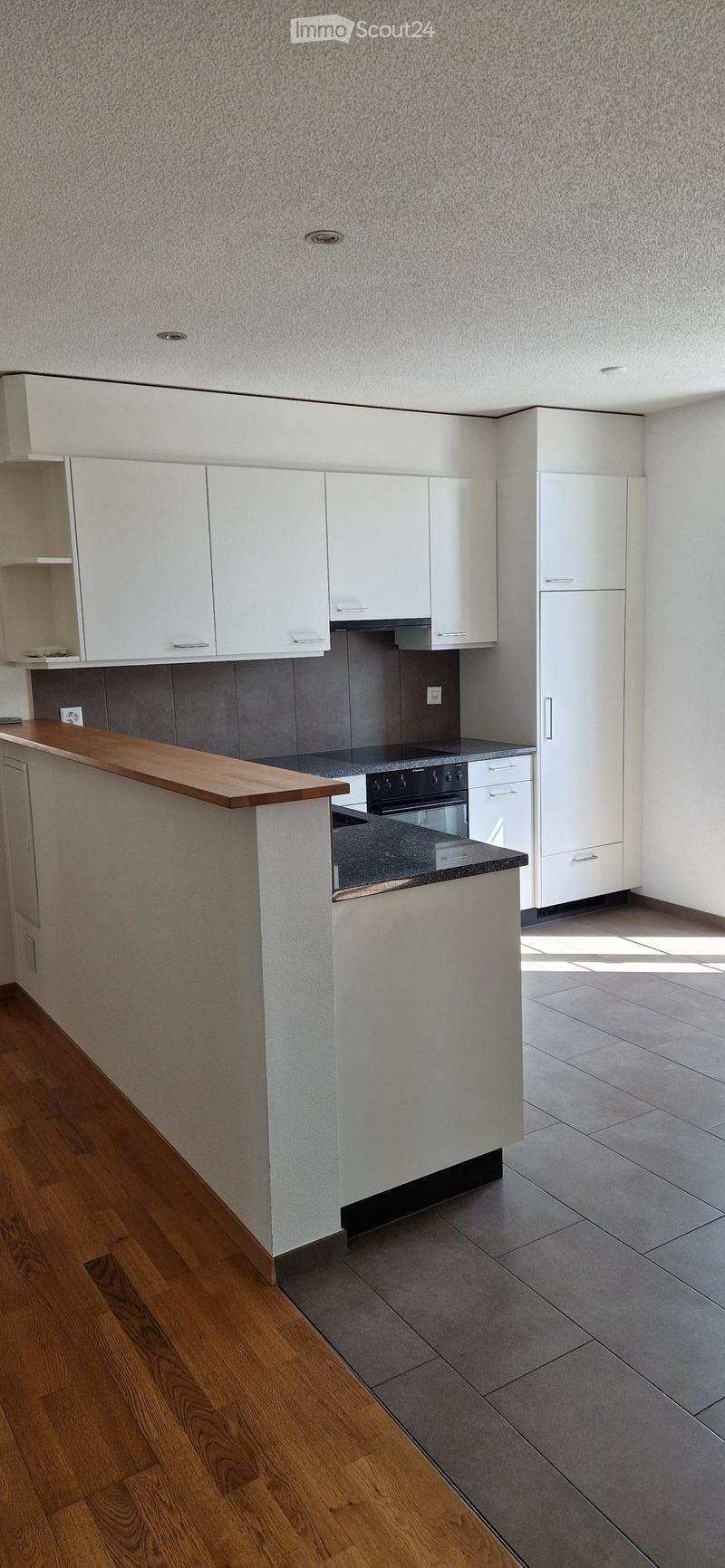 Modern kitchen with white cabinets, wooden countertop, and grey tiled backsplash. Features an oven and ample storage space.