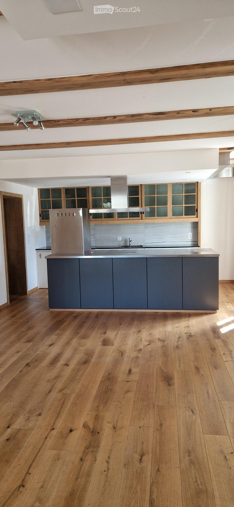 Modern kitchen with wooden flooring, dark grey cabinets, stainless steel appliances, and a central island with a sink and faucet.