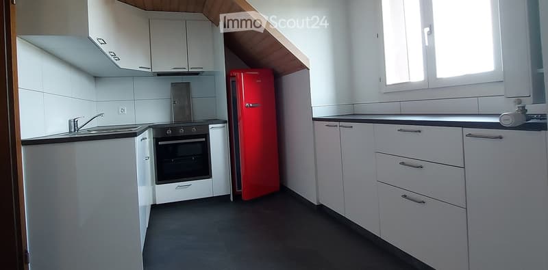 Modern kitchen with white cabinets, black countertops, stainless steel sink, oven, and red refrigerator. Features a window and sleek design.
