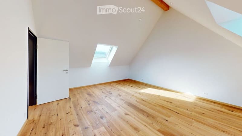 Empty attic room with wooden flooring, white walls, and skylight windows.