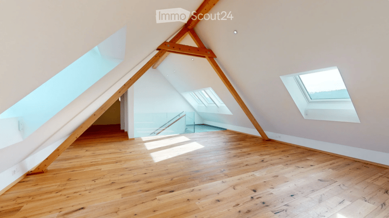 Bright, empty attic room with wooden flooring, exposed wooden beams, and skylights allowing natural light to flood the space.