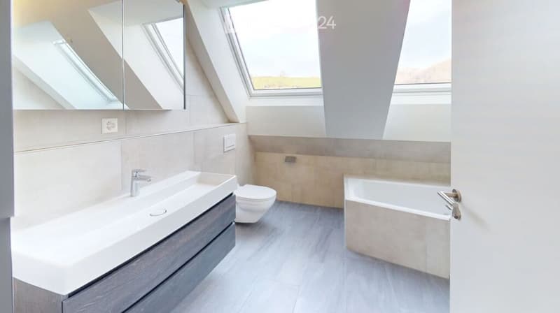 Modern bathroom with a large sink, toilet, bathtub, and large windows with skylights. The walls are tiled in neutral tones, and the floor is wooden.