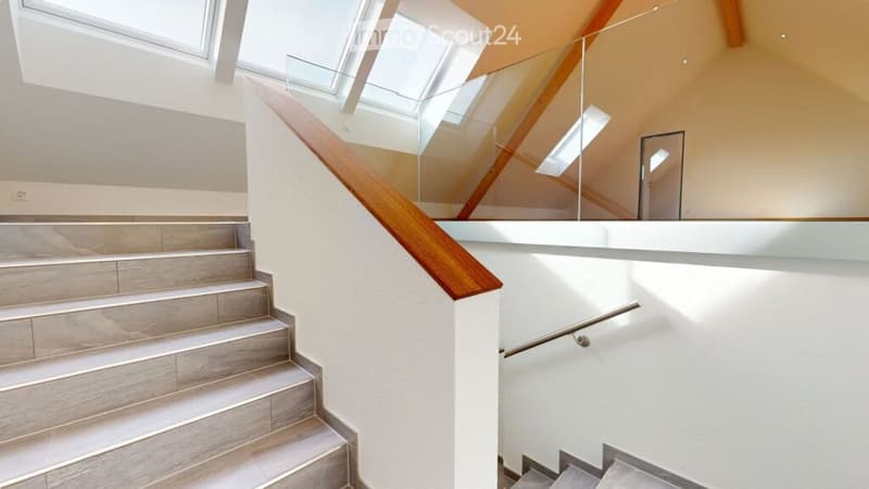 Modern interior staircase with wooden steps, glass railing, and skylight windows providing natural light.