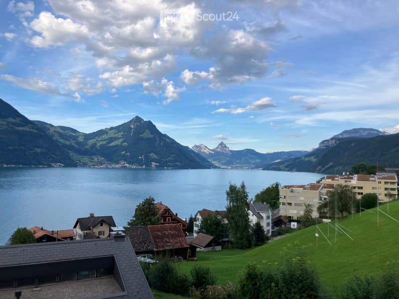 A scenic view of a lake surrounded by mountains, with a small village of houses and trees in the foreground.