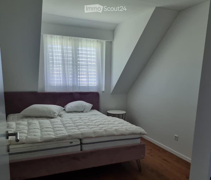 Cozy attic bedroom with a double bed, white bedding, and a small round nightstand near the window.