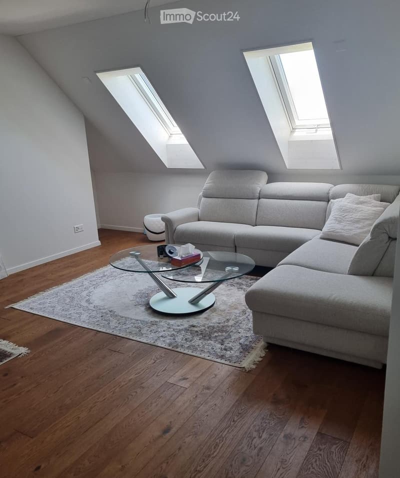 Modern living room with wooden flooring, grey sectional sofa, glass coffee table, and a patterned rug.