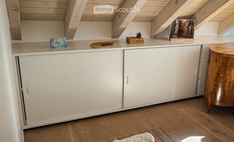 A small, modern room with white cabinets, a wooden stool, and various decorative items on the counter, including a picture frame, a book, and a small wooden box.